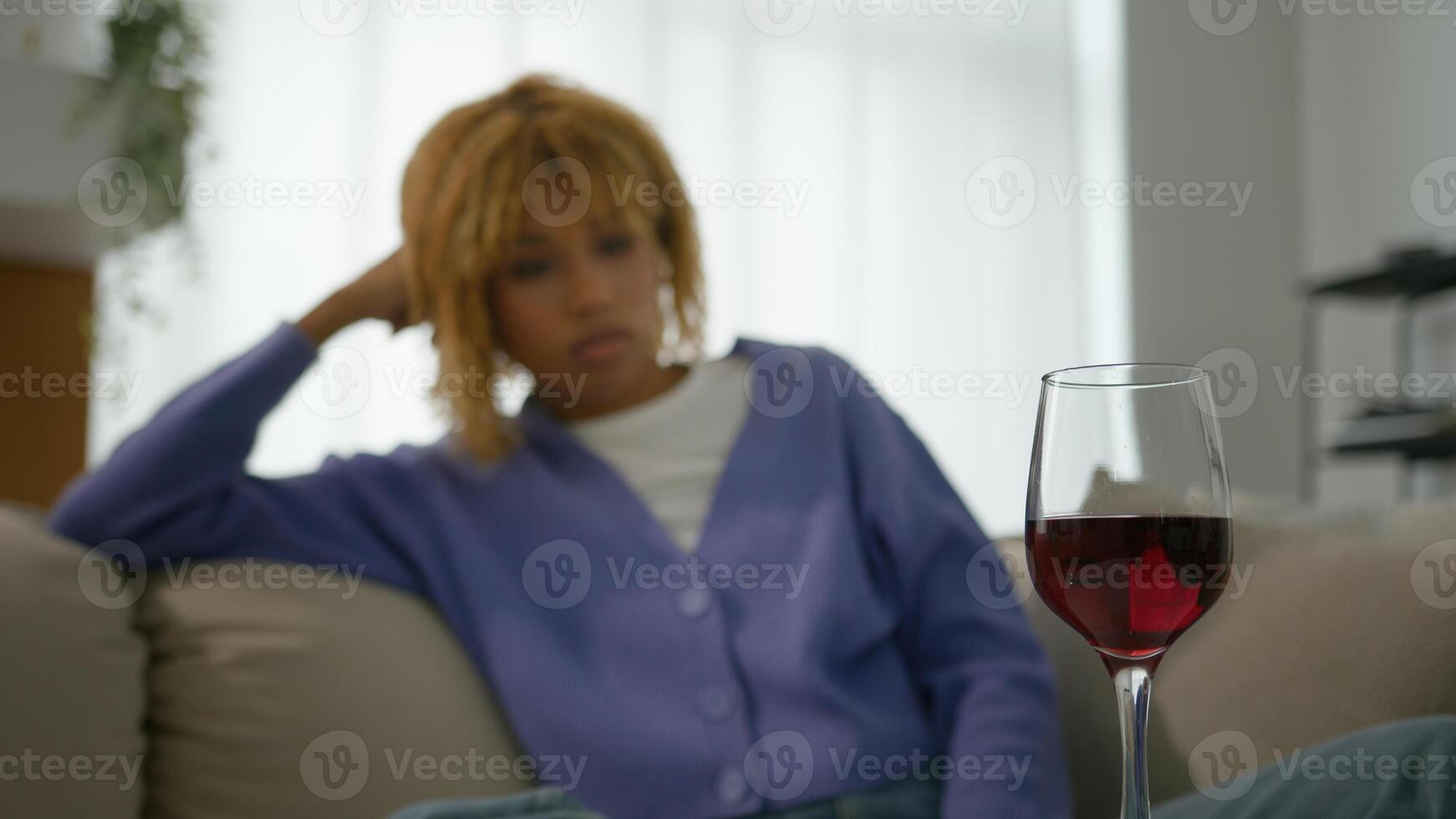 Sad upset lonely ethnic African American girl pensive thoughtful woman think alone thinking at home relaxing at living room couch sofa looking at glass of red wine alcohol addiction relax depression photo