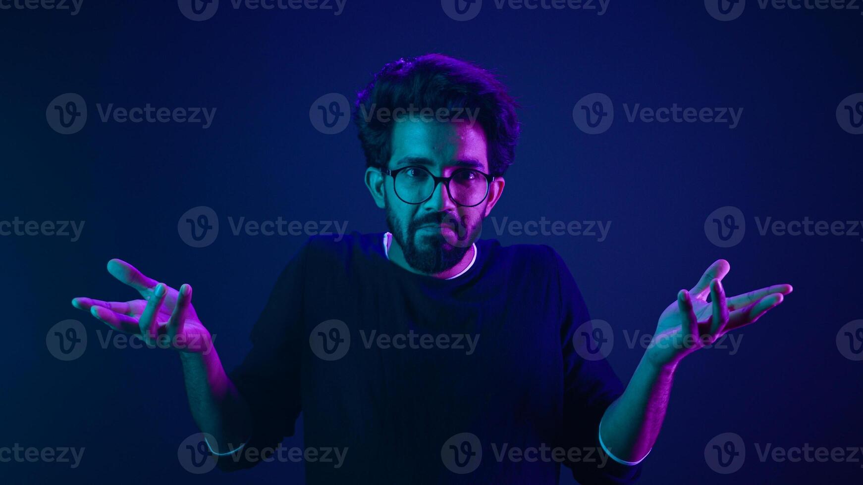 Studio dark blue neon background Indian man Arabian male model guy confused shrug shoulders unsure doubtful shrugging doubt uncertain don't know problem solution question guess puzzled bemused no clue photo