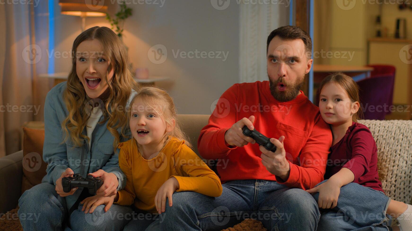 Funny children parents Caucasian happy family play game online at home weekend mom dad kids little girls daughters addicted playing console with joysticks have fun gaming entertainment together photo
