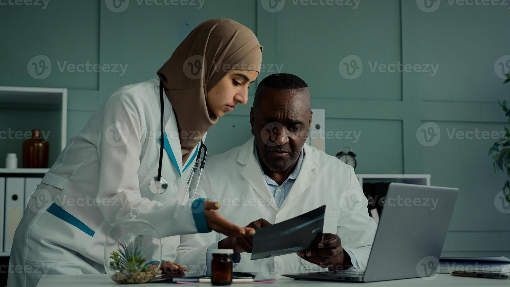 Multiracial doctors colleagues discuss teamwork african man and arabian woman two professional medical workers talk about healthcare check MRI scan use computer app doing online research X-ray results photo
