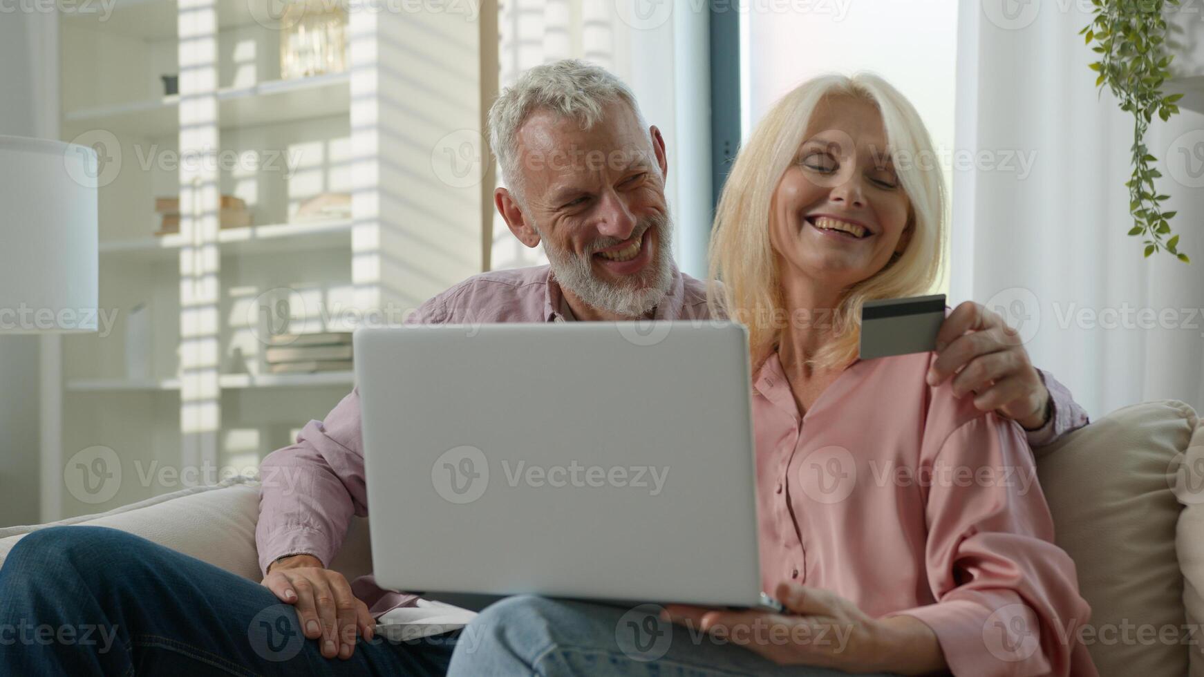 Happy elderly married couple man woman customers hugging making purchase online using laptop talking at home together remote paying with credit card safe instant payment on internet e-banking service photo