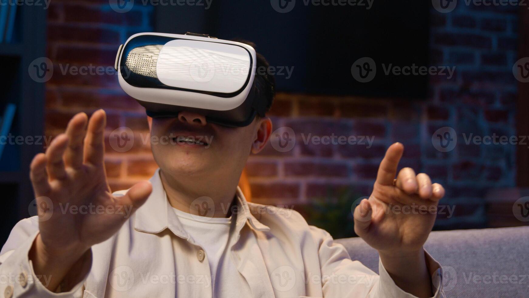 Asian man play game virtual reality experience cyberspace world modern technology explore 3d goggles eyeglasses at night home Korean male in VR glasses helmet play simulation at evening at couch photo