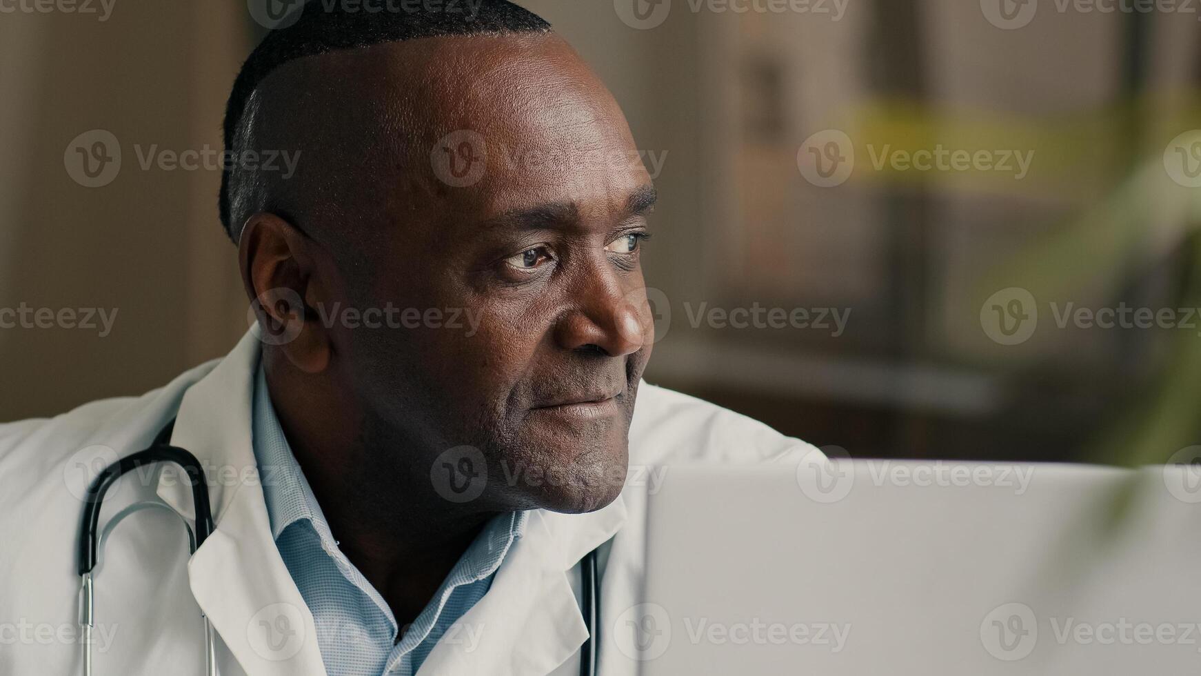 Happy middle-aged man doctor positive medical worker sits at hospital clinic cheerful smiling makes approval hand gesture okay agree winks one eye good recommendation satisfied with healthcare service photo