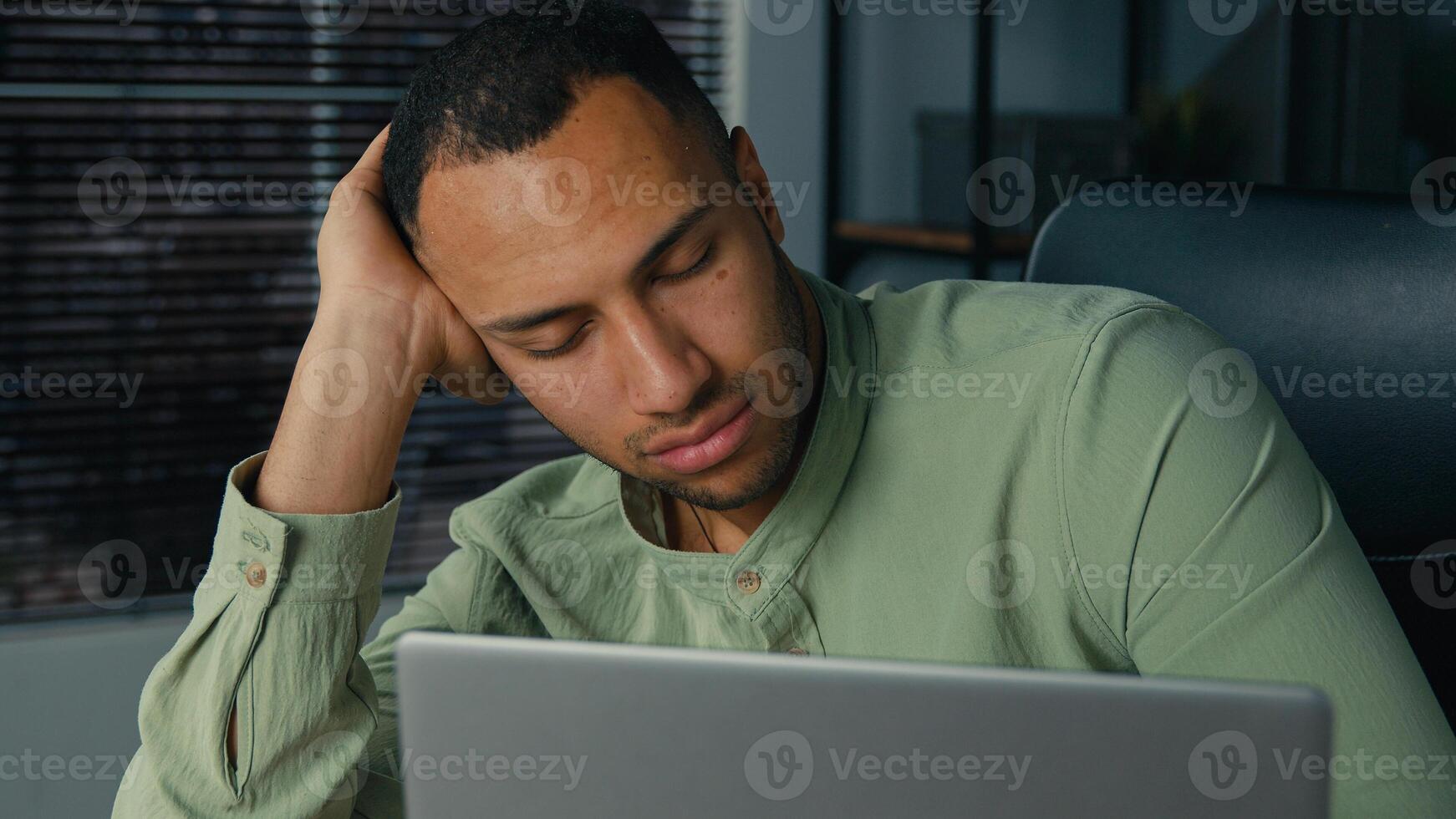 Tired lazy young african american businessman bored at work fall asleep at office desk sleepy overworked ethnic man employee sleeping at workplace near laptop napping resting feel exhaustion fatigue photo