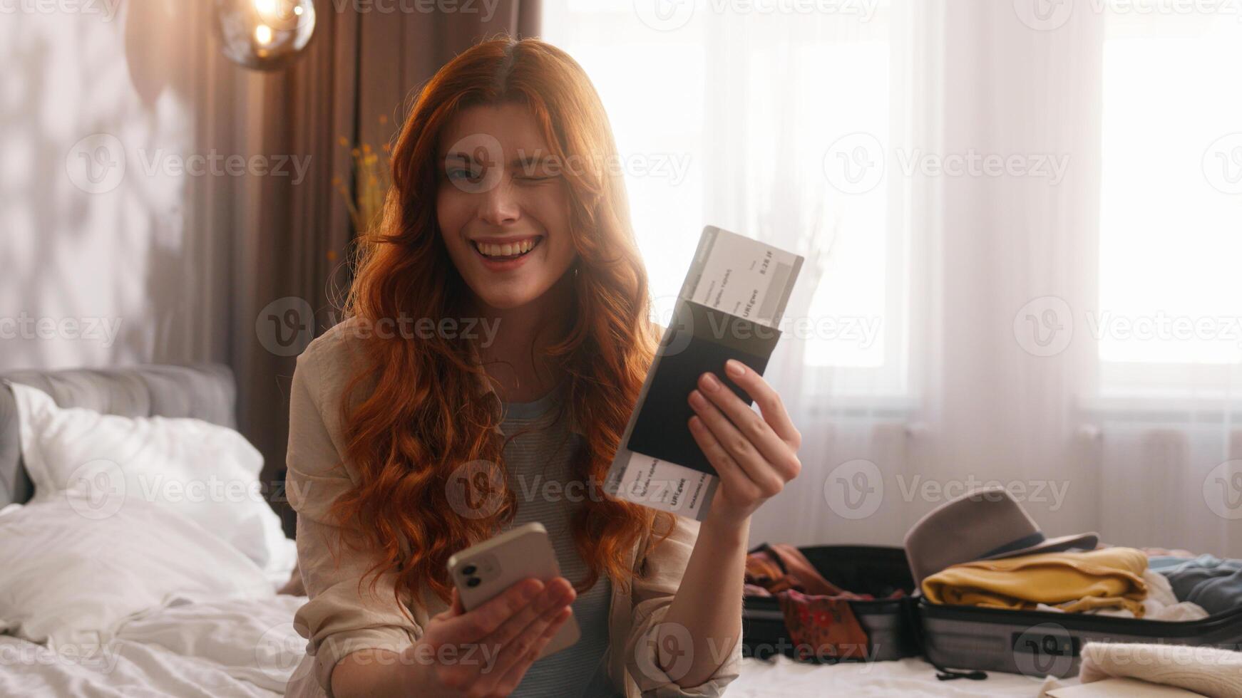 Caucasian woman female girl traveler tourist lady happy smiling at home bedroom hotel prepare for trip travel vacation tour journey packing suitcase hold mobile phone tickets passport smile at camera photo