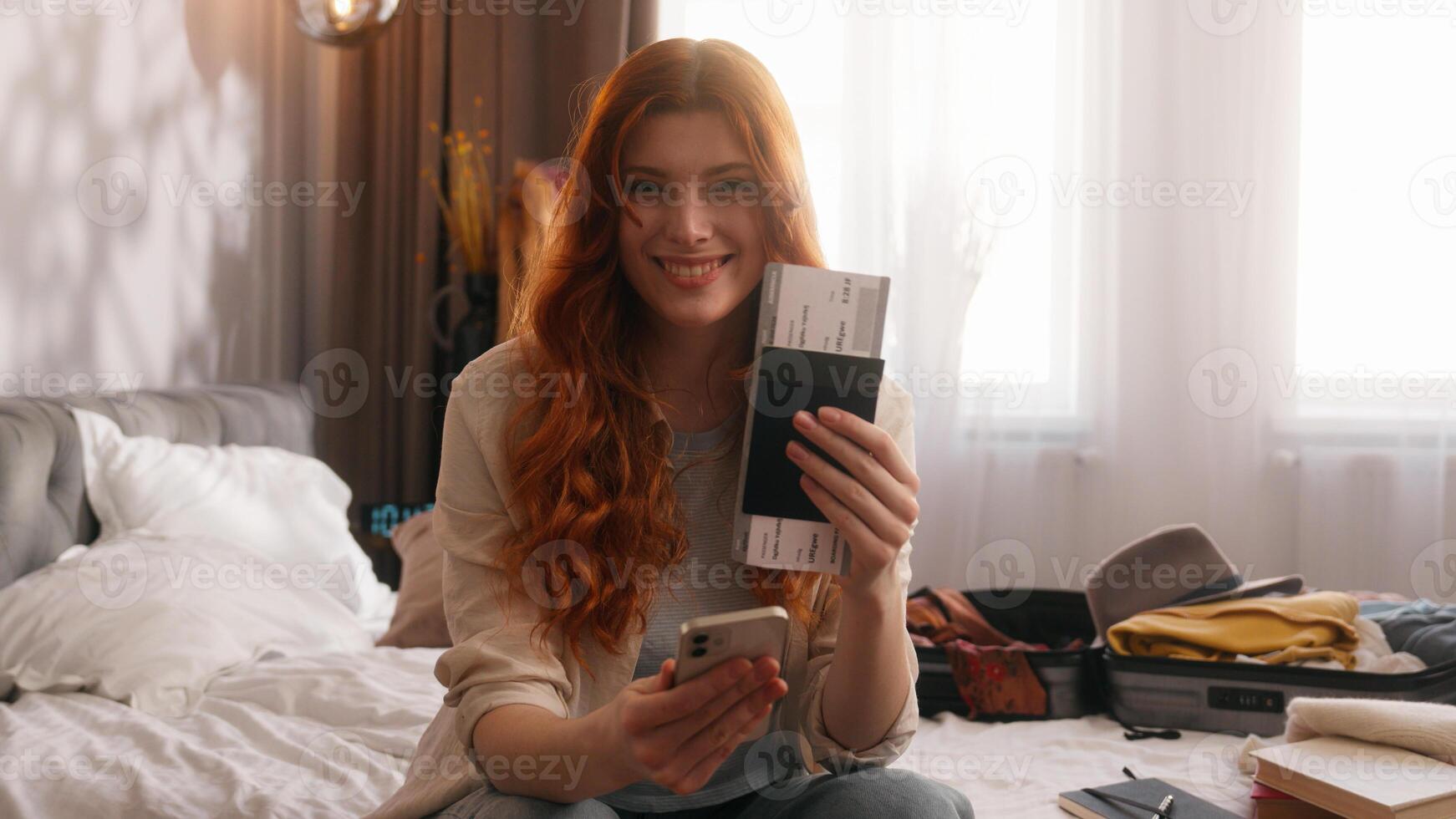 Caucasian woman female girl traveler tourist lady happy smiling at home bedroom hotel prepare for trip travel vacation tour journey packing suitcase hold mobile phone tickets passport smile at camera photo