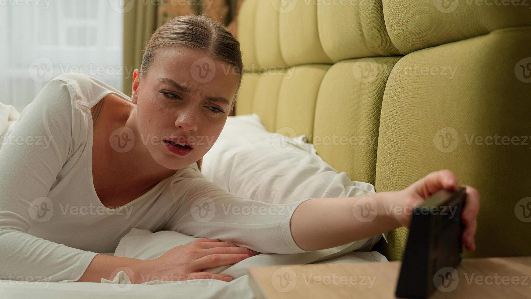 Tired sleepy fatigued girl wake up in early morning bed home bedroom stressed dissatisfied upset lazy time go work insomnia health problem sleep disorder woman female lady loud ringing of alarm clock photo