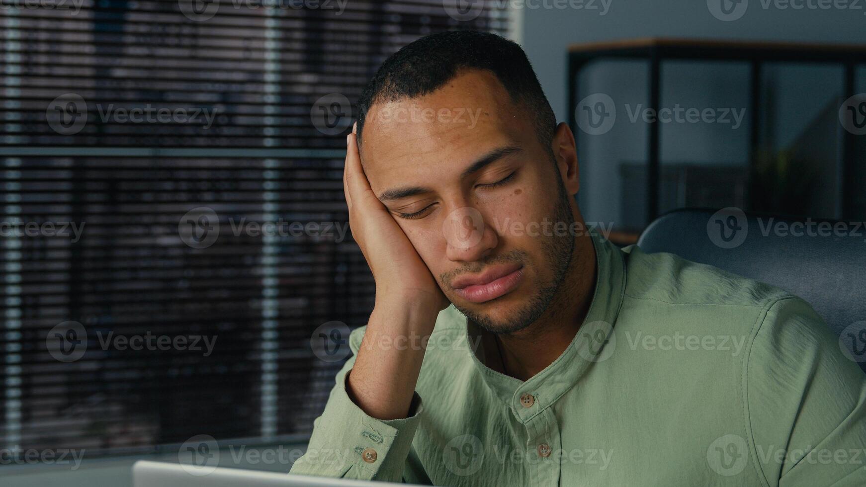 Tired lazy young african american businessman bored at work fall asleep at office desk sleepy overworked ethnic man employee sleeping at workplace near laptop napping resting feel exhaustion fatigue photo