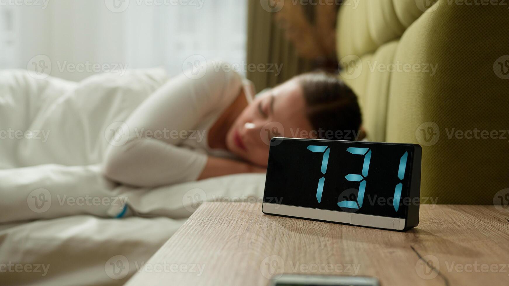 Angry annoyed tired exhausted girl wake up in morning bed home bedroom woman female lady anger mad furious loud sound ringing of alarm clock awaking early beat off alarmclock continue sleep insomnia photo