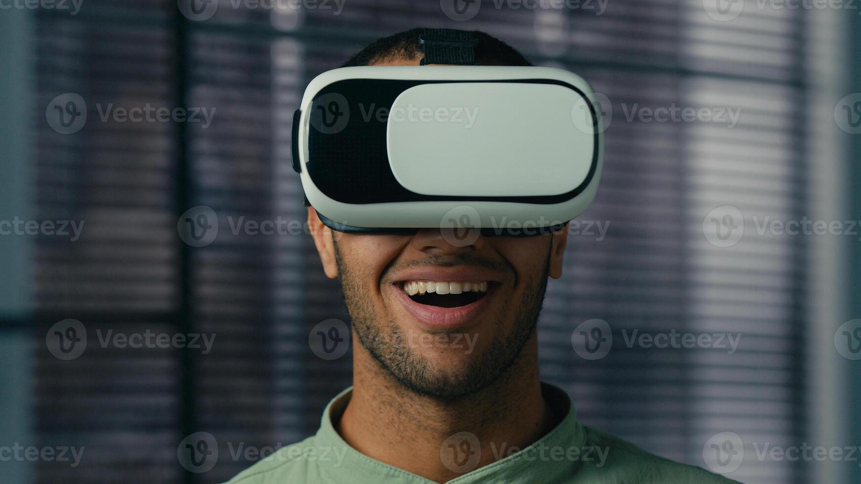 Close-up smiling latin american man wearing virtual reality glasses friendly showing invitation gesture asking to come welcome symbol making choice male player playing in cyberspace with vr goggles photo