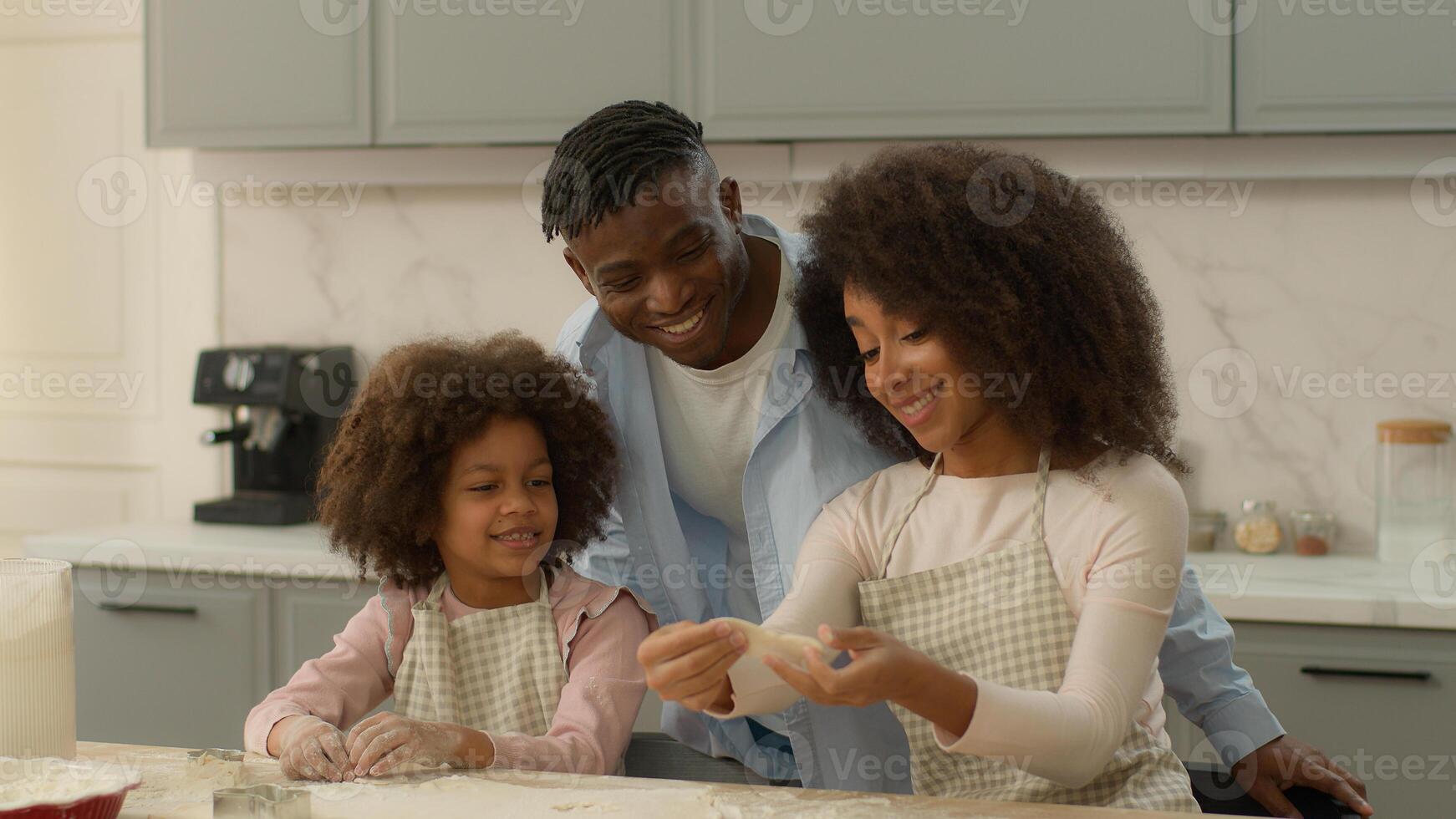 Happy African American family at home kitchen woman man and little girl father cuddling hugging child kid daughter mother show dough flour cooking cookies cook baking pastry together talking insurance photo