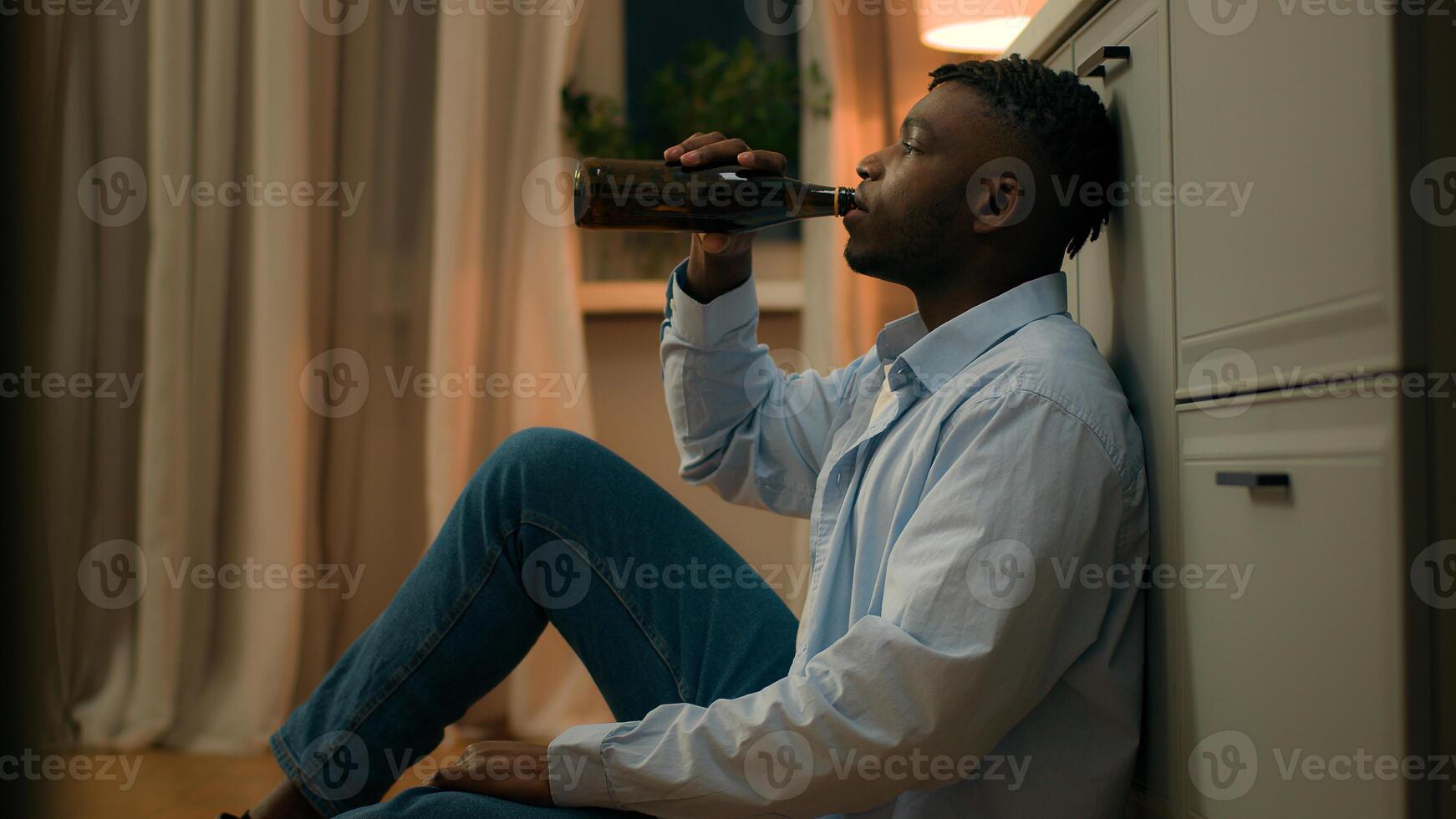 Sad upset African American man drunk male addicted guy alcohol addiction drinking beer alone at home kitchen evening on floor suffer heartbreak divorce health problem alcoholism bankruptcy loan lost photo