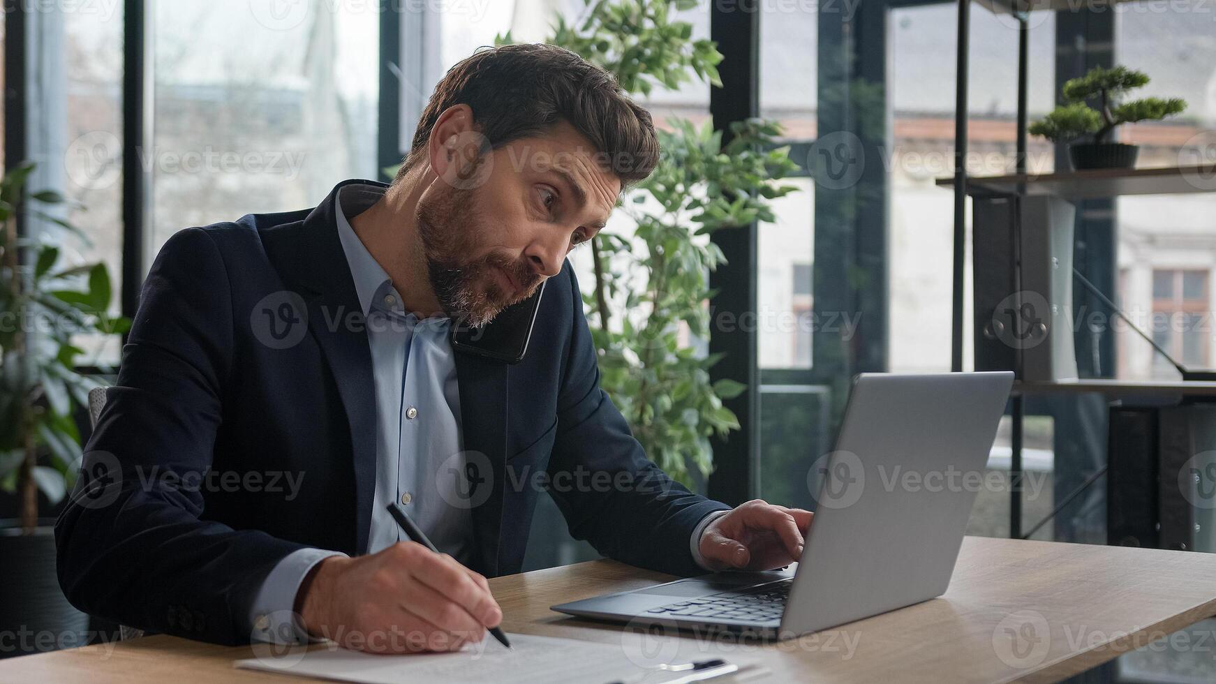 Busy successful caucasian adult businessman in office typing on laptop talking to client on mobile phone writing notes explain condition multitasking man manager communicate on cellphone in workplace photo