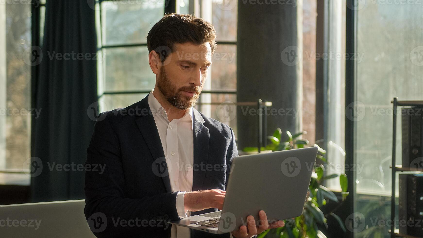 Successful caucasian businessman typing on laptop working on Internet in office in morning sunshine adult happy man leader boss professional manager model smiling looking camera posing at workplace photo