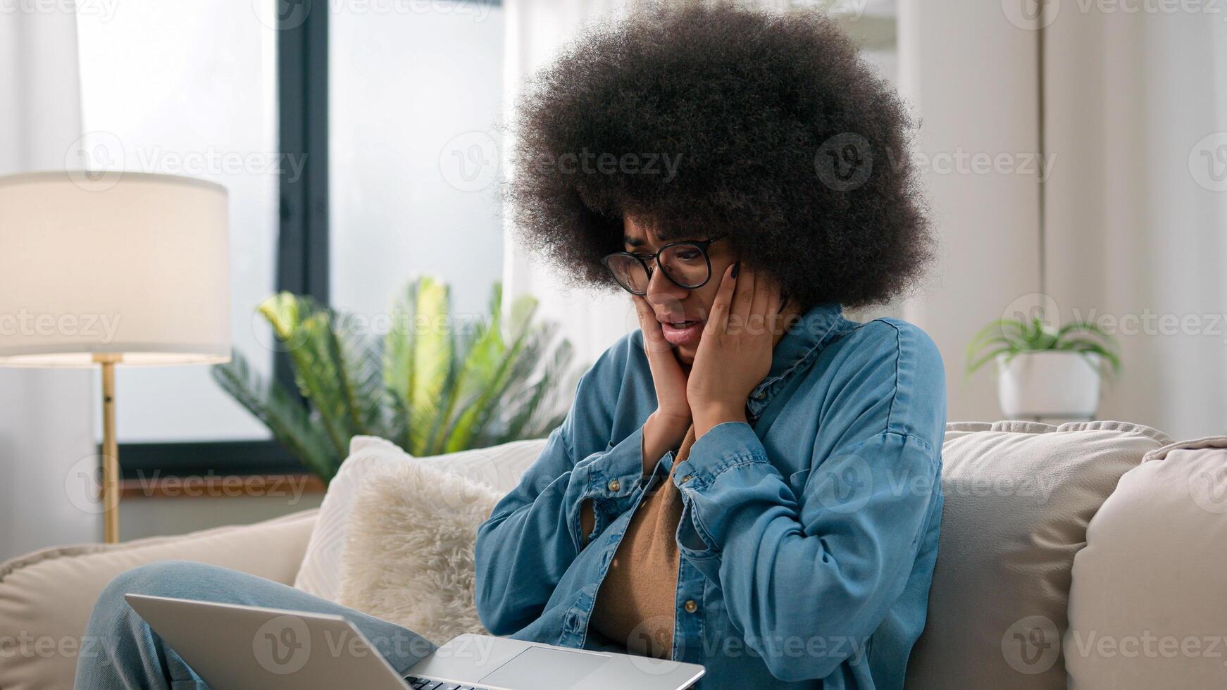 Sad upset shocked anxious worried confused African American woman ethnic girl shock failure lost with laptop bad news computer error mistake refuse notification bank problem exam failing at home sofa photo