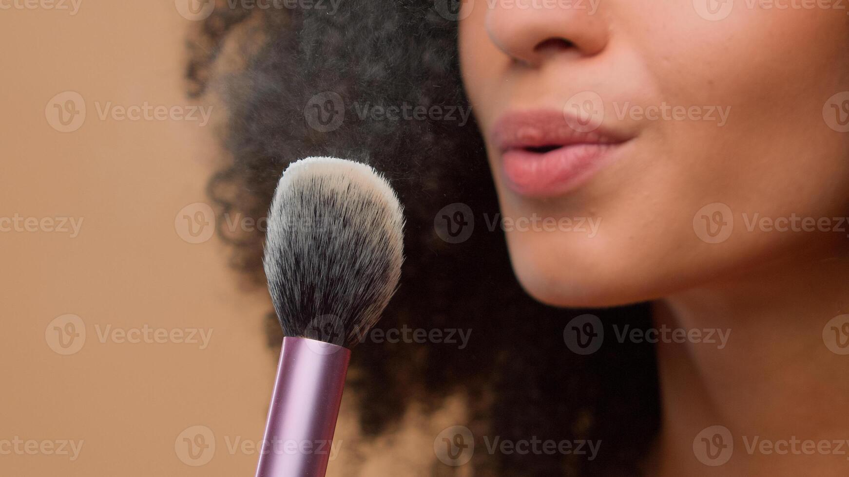 Cosmetic make-up beauty concept close-up cropped view unrecognizable African American woman unknown model girl holding brush blow away dust apply skin tone powder at beige studio background skincare photo