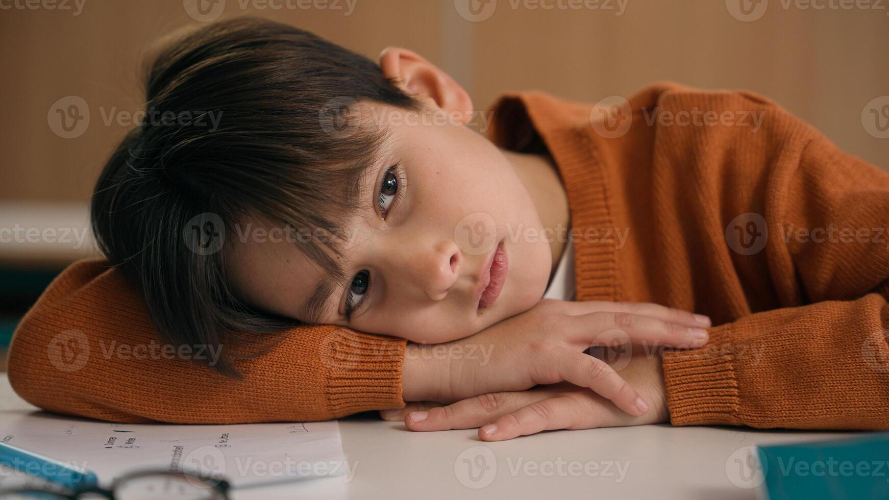 Caucasian bored schoolboy sleepy at school elementary education study learning tired exhausted sad upset fatigued child boy kid pupil schoolchild lying at table desk lesson class relax health problem photo