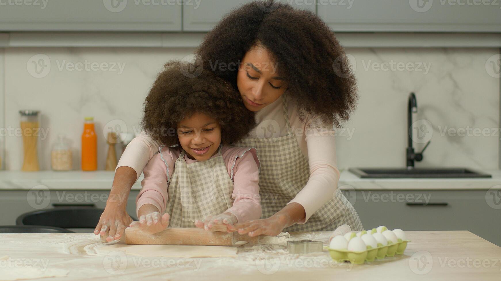 Family cooking together at kitchen African American care mother showing how flattening flour dough mom help teach little daughter child cook cookie pie cake pizza helping kid girl use one rolling-pin photo