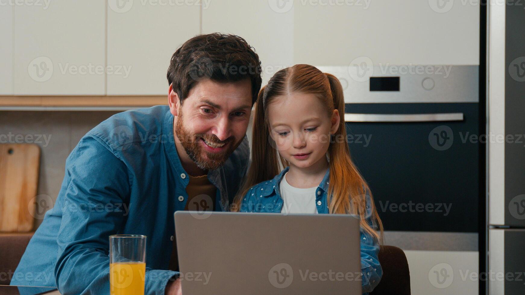 Adult dad explain teaching small kid girl help with using laptop at home kitchen. Daughter learning typing surfing browsing internet with parental control using modern computer together with father photo
