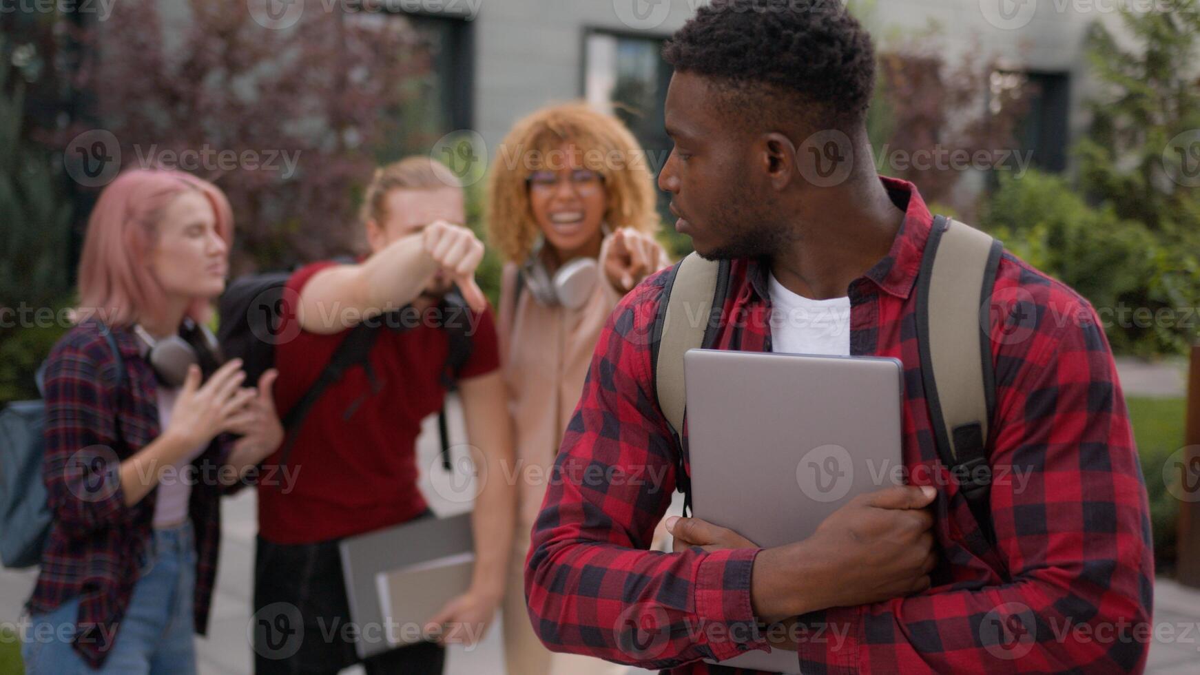 Sad upset offended victim boy student guy African American suffering man bullied of group multiracial students teens classmates thumb down mocking bully abused bullying university college aggression photo