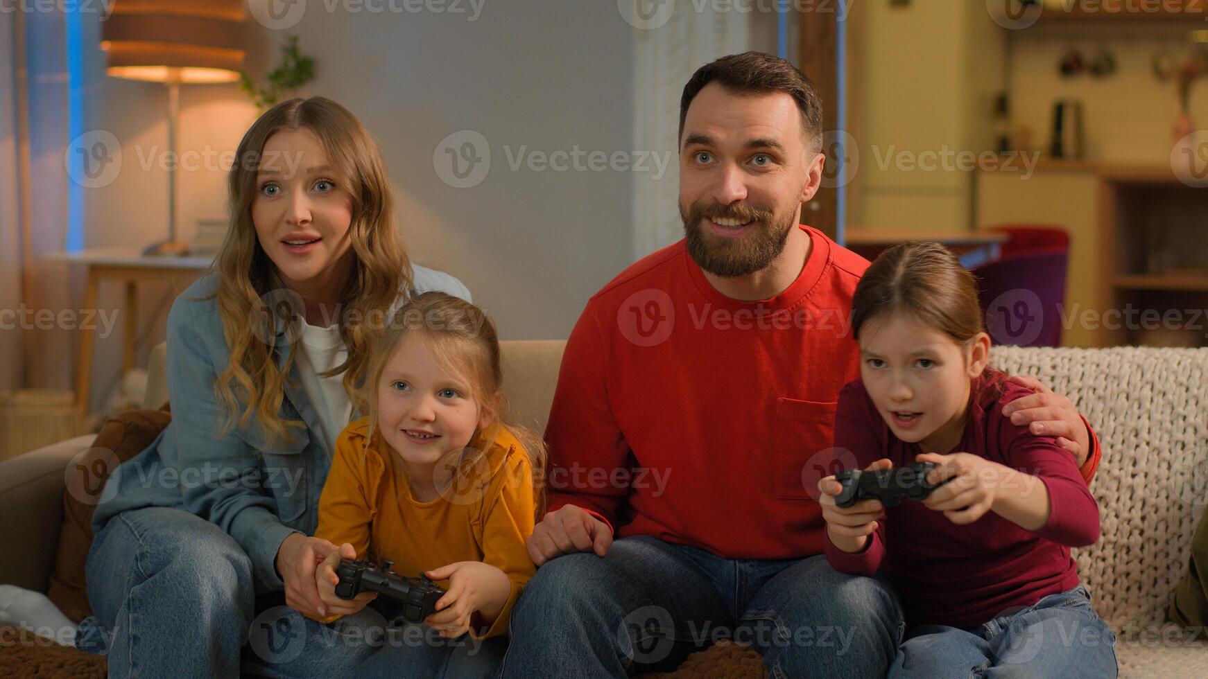 Funny children parents Caucasian happy family play game online at home weekend mom dad kids little girls daughters addicted playing console with joysticks have fun gaming entertainment together photo