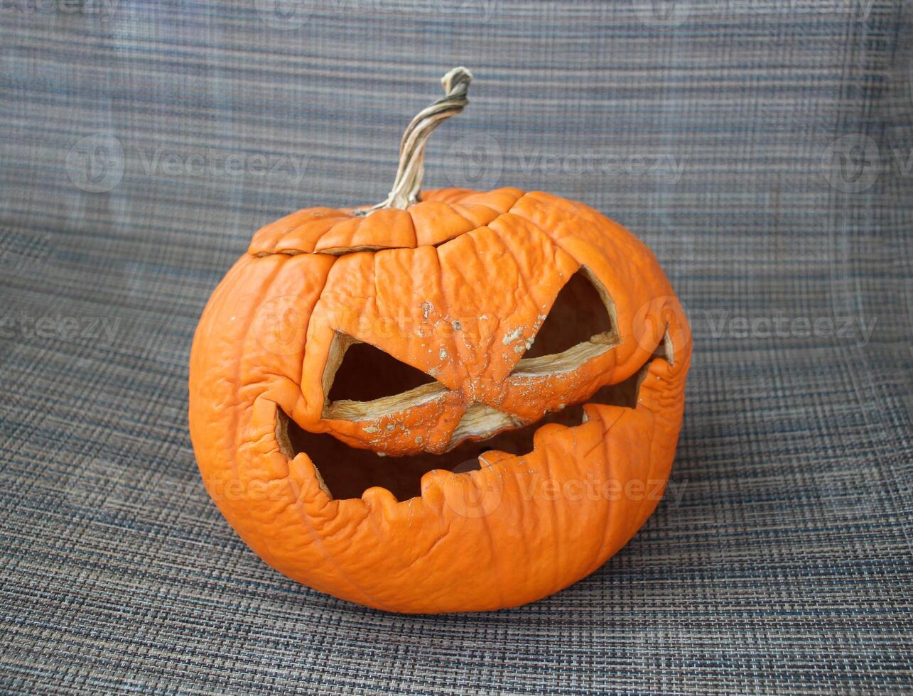 Wrinkled carved pumpkin with a spooky expression on a fabric background. photo