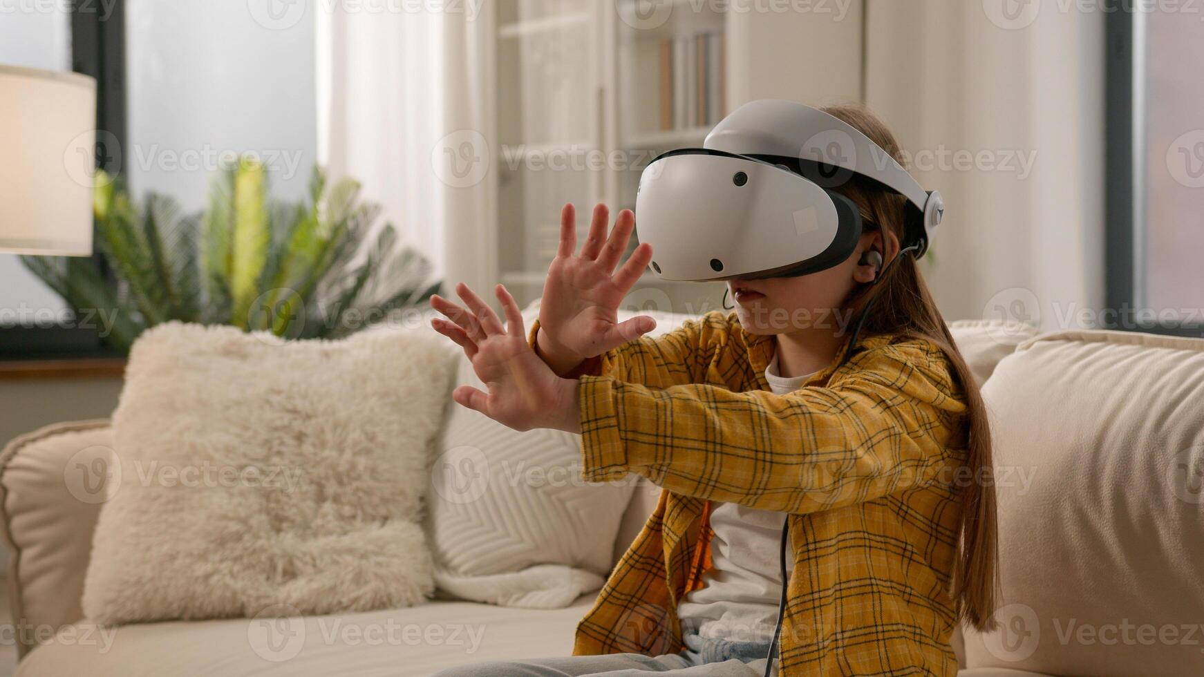 Funny caucasian kid girl child schoolgirl having fun in virtual reality headset at home couch playing online game in world metaverse using innovative technology VR glasses exploring cyberspace photo