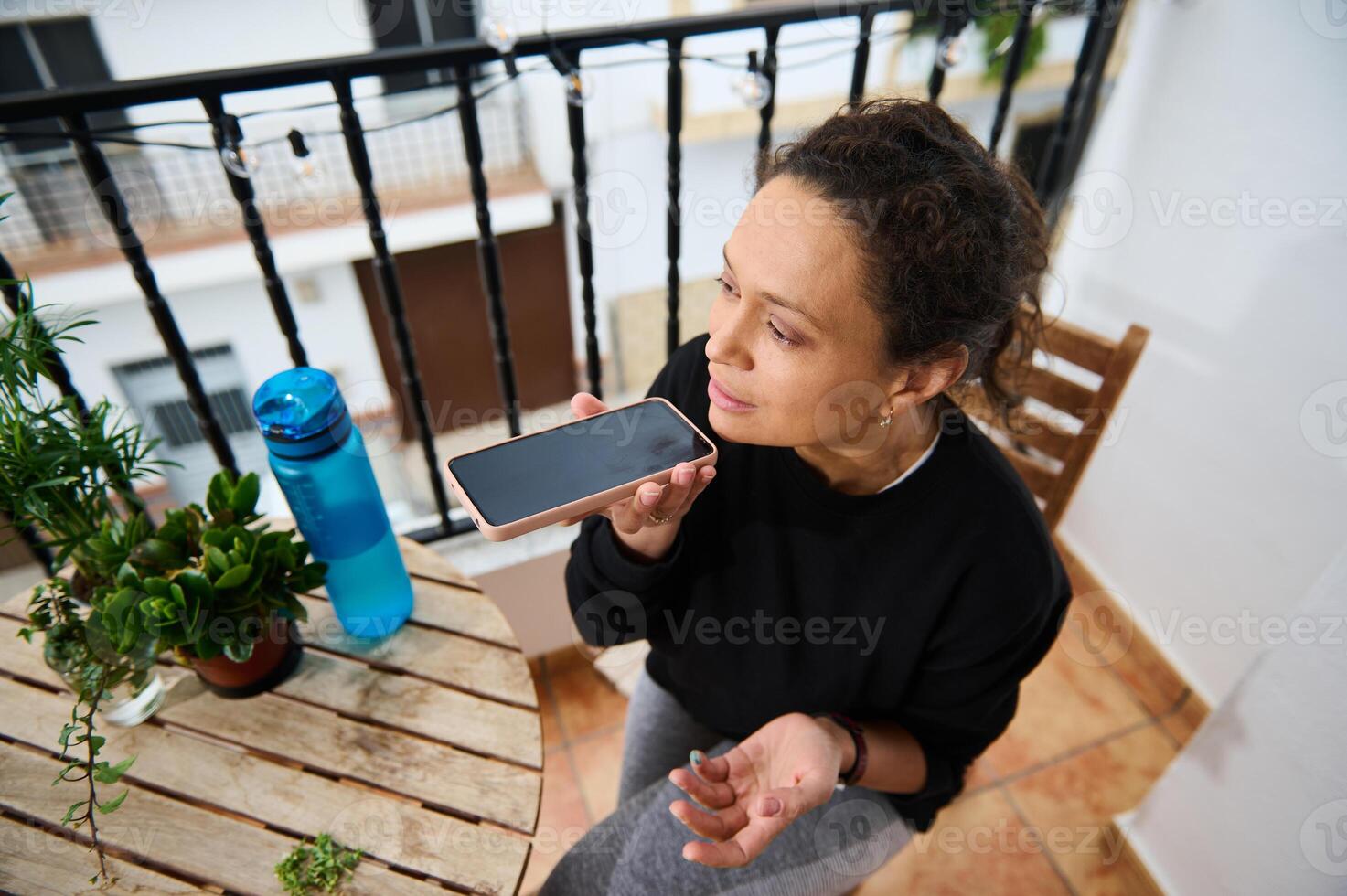 Woman using voice assistant on smartphone outdoors on balcony photo