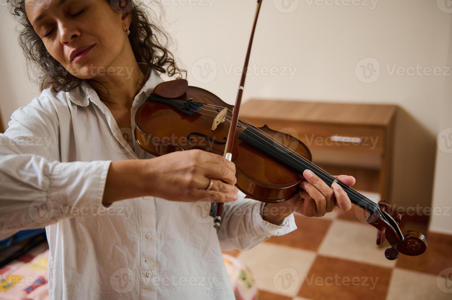Woman playing violin with closed eyes in peaceful home environment photo