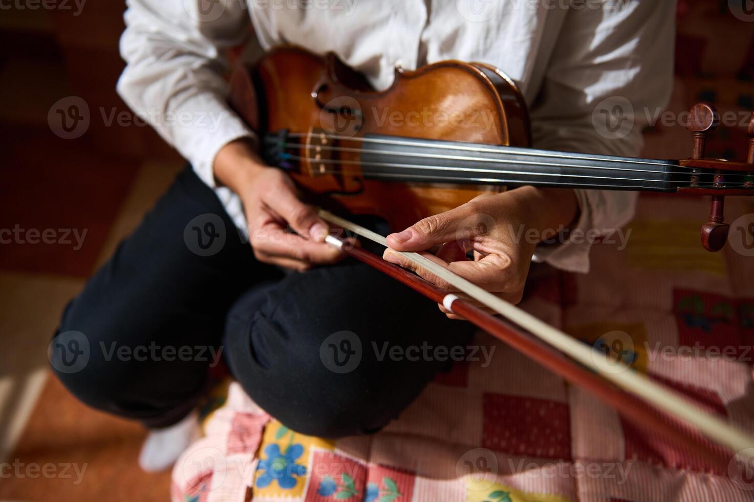 Person adjusting violin bow on a colorful quilted surface photo