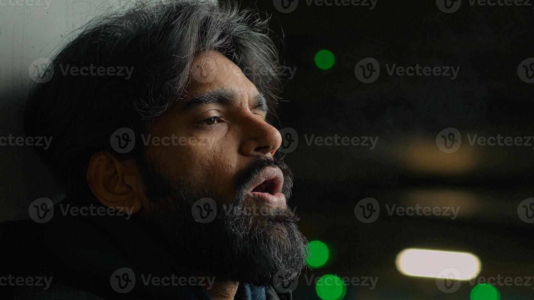 Helpless homeless Indian depressed stressed bearded man suffer at dark parking lot city night froze Arabian stressful grief sad upset guy exhale steam frozen breath frosty smoke cold temperature flue photo
