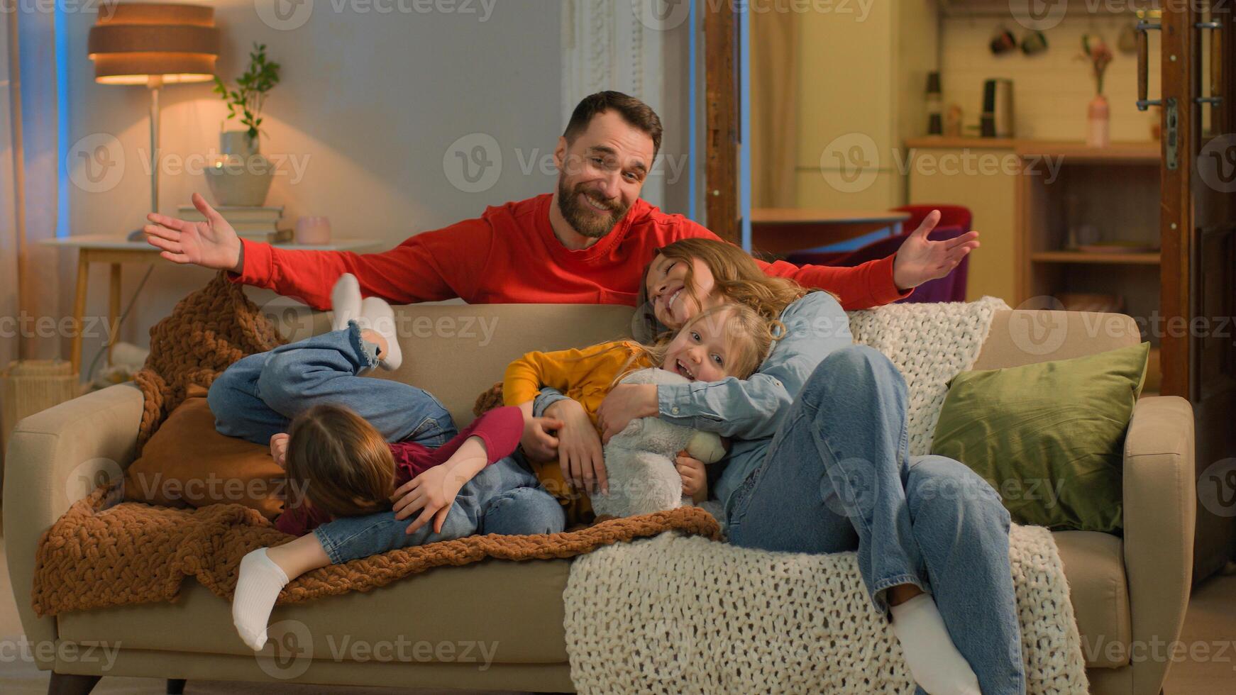 Caucasian family happy joyful children parents mom dad little girls daughters running jumping on sofa carefree funny mother father love kids cuddle hug on couch weekend home laugh smile unity portrait photo