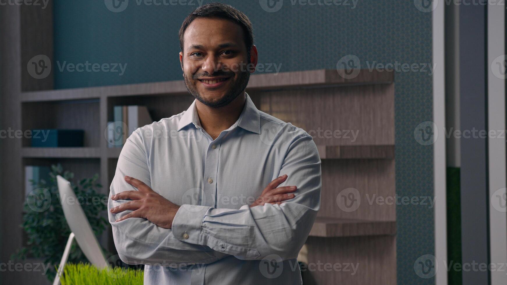 Business portrait in office adult Indian man American guy ethnic businessman entrepreneur employer with hands crossed posing at workplace modern marketing company hr manager worker smiling at camera photo