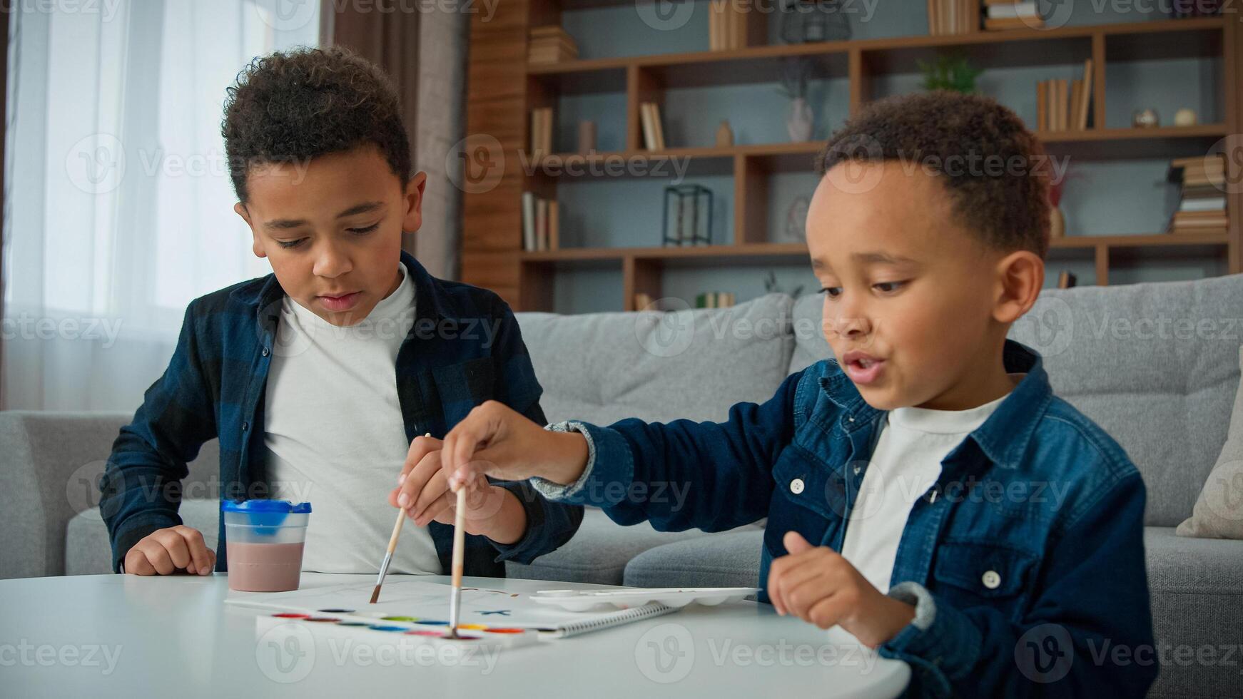 Two little children boys painting at home together. Ethnic brothers African American kids sibling paint picture with acrylic watercolor colors schoolboys indoors enjoy art hobby with paintbrushes photo
