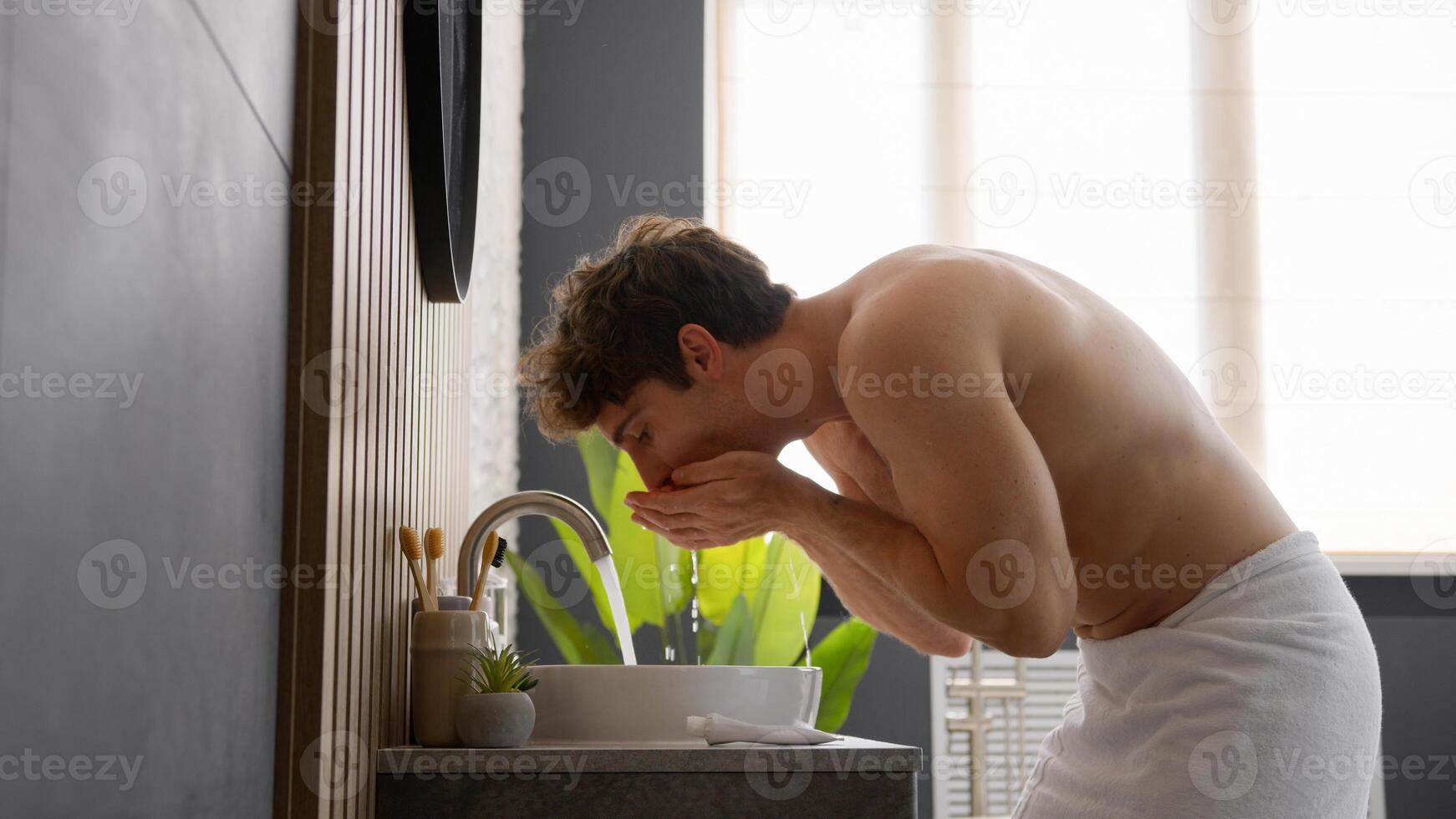 Caucasian handsome male naked guy man brushing teeth in bathroom cleaning tooth doing oral mouth hygienic daily refreshing toothy morning procedure toothcare dental care looking at mirror in bathroom photo