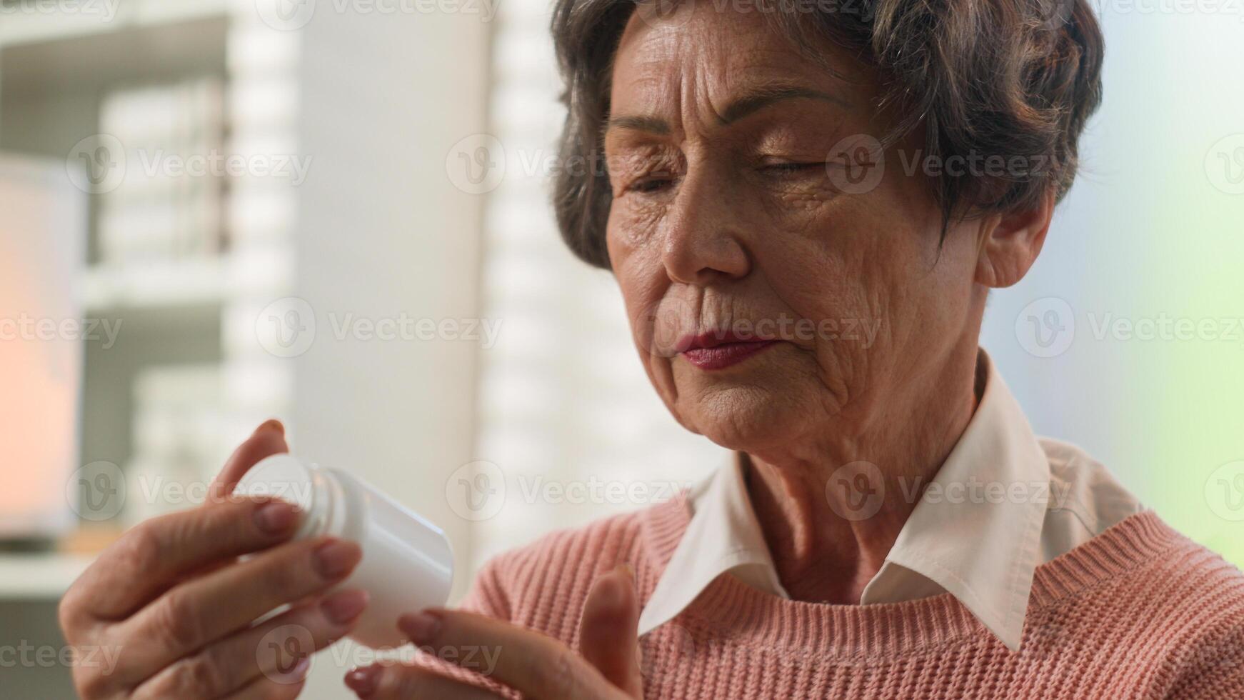 Caucasian grandmother senior woman at home old female elderly granny retired lady holding jar of pills dose remedy painkiller reading name of medication Alzheimer diabetic healthcare medicine concept photo
