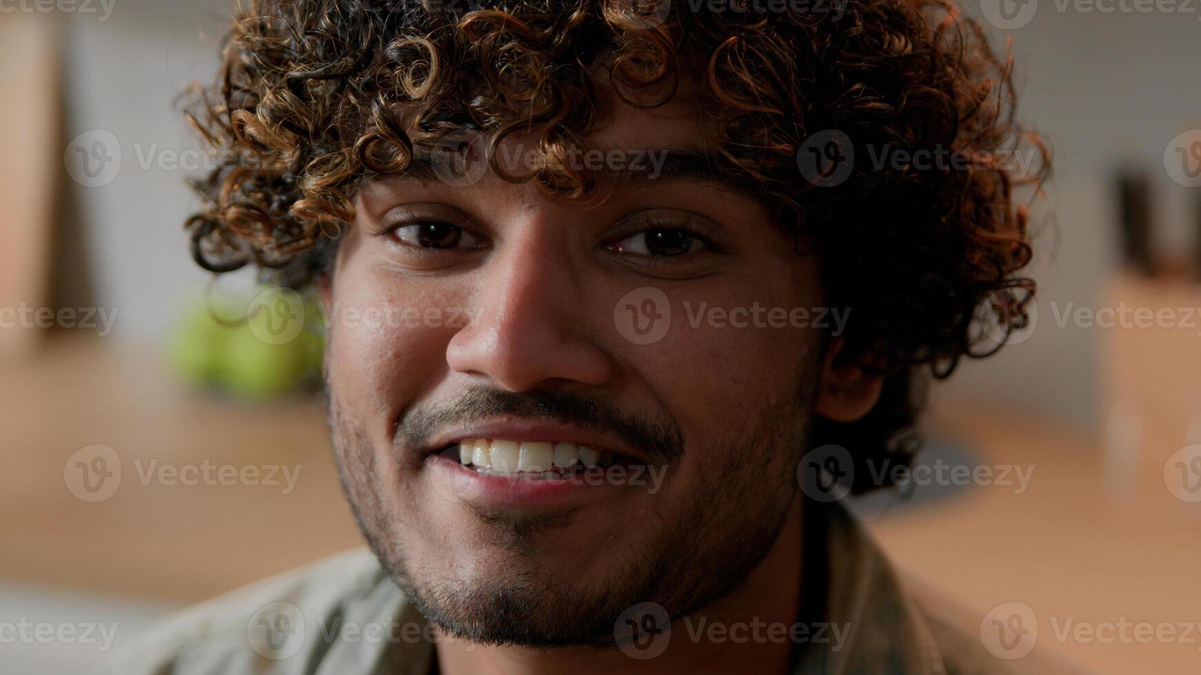 Close up smiling Arabian man homeowner with curly hair vlogger look at camera at kitchen. Portrait Indian male face with smile indoors. Headshot ethnic guy business conference call web cam view photo