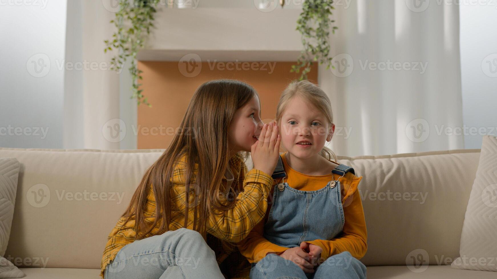 Two caucasian kids girls children sisters friends playing together at home older sister telling little girl news whispering in ear speak in whisper sharing secret gossip family relationship friendship photo