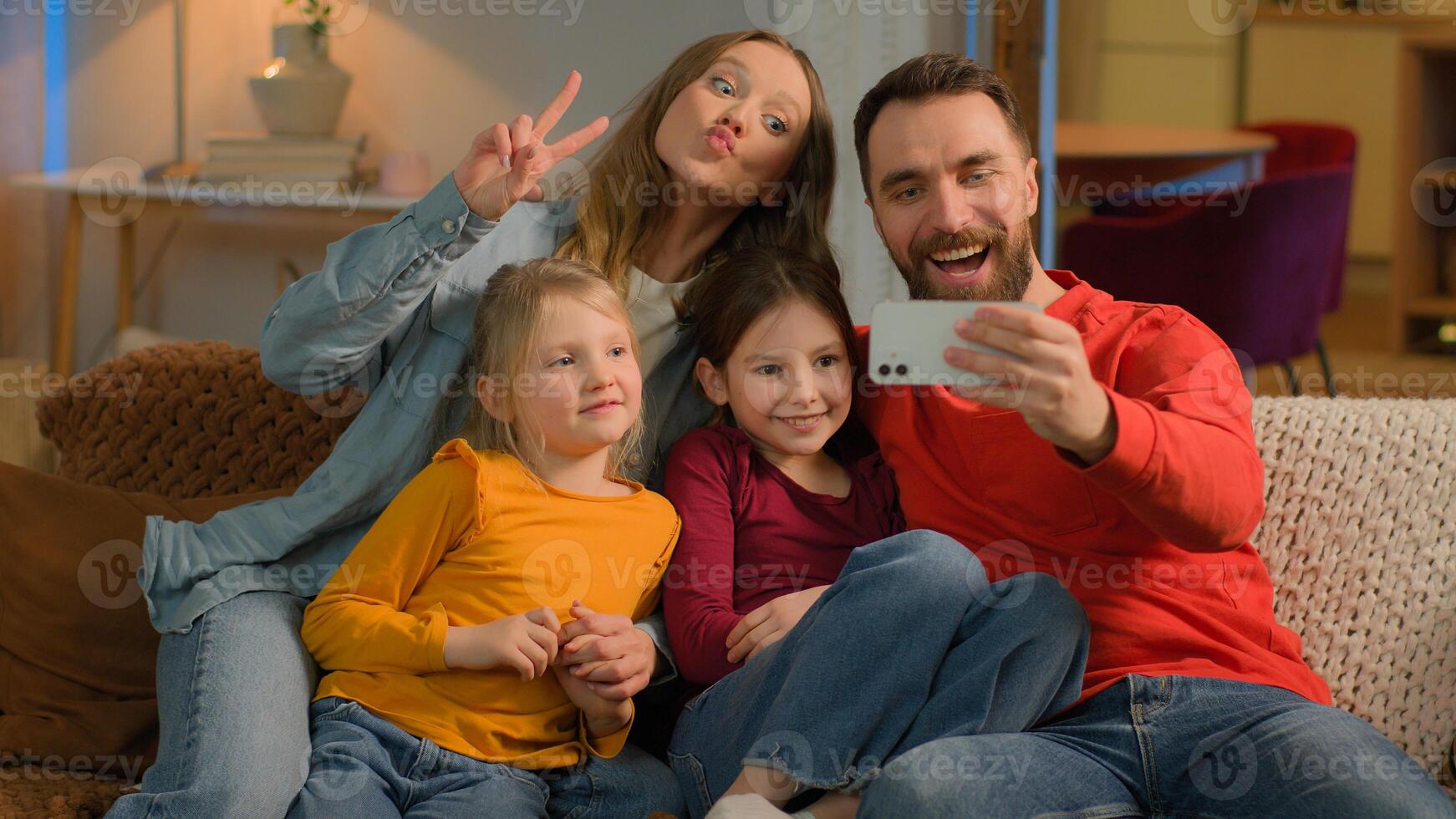 Caucasian happy family mother father kids little girls daughters posing grimace photo on mobile phone at evening home funny parents children record online blog smartphone selfie social media app