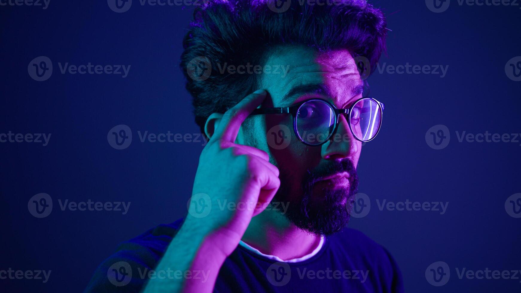 Indian man developer coding worker computer smart clever hacker in glasses neon ultraviolet studio background thinking hard brain power mental strength think about it ponder problem solving IQ gesture photo