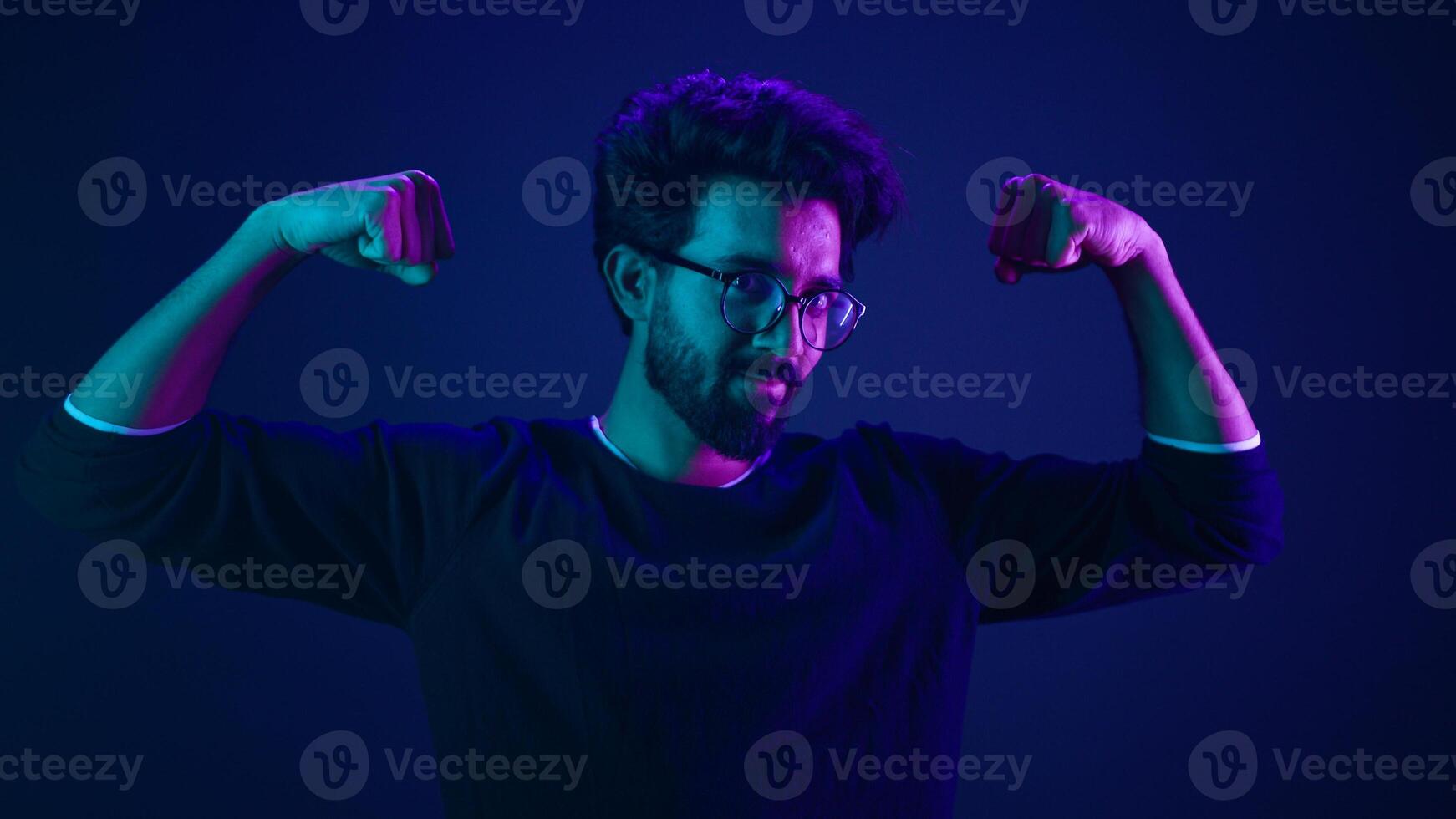 Proud slim weak Arabian man coder guy technology hacker show hands muscle bicep sport strong power like bodybuilder neon studio background champion boast efficient security coding achievement level up photo