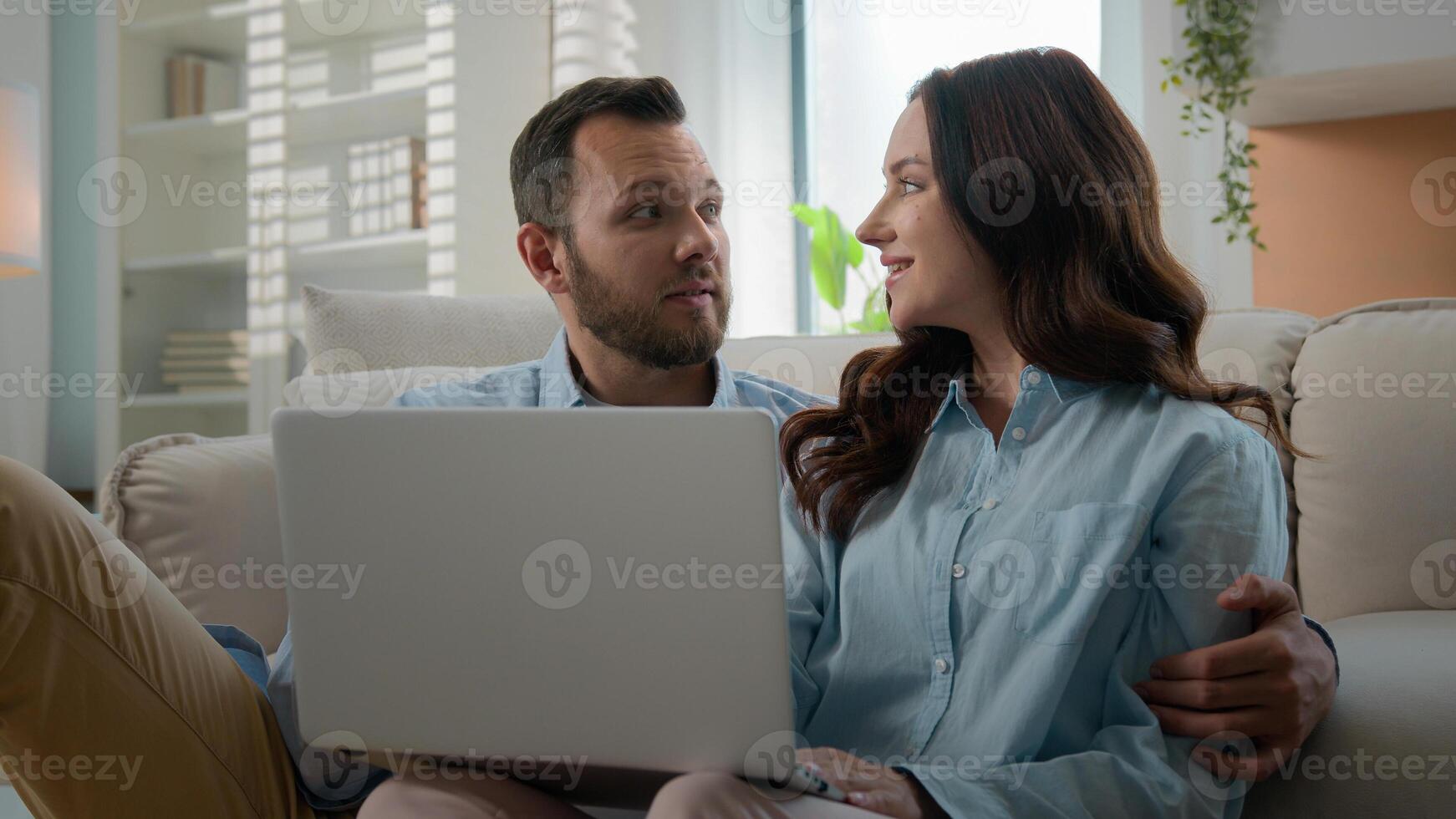 Happy young couple using laptop for ecommerce doing online shopping with shop app together at home Caucasian man and woman looking at computer buying searching in internet booking trip tickets choose photo