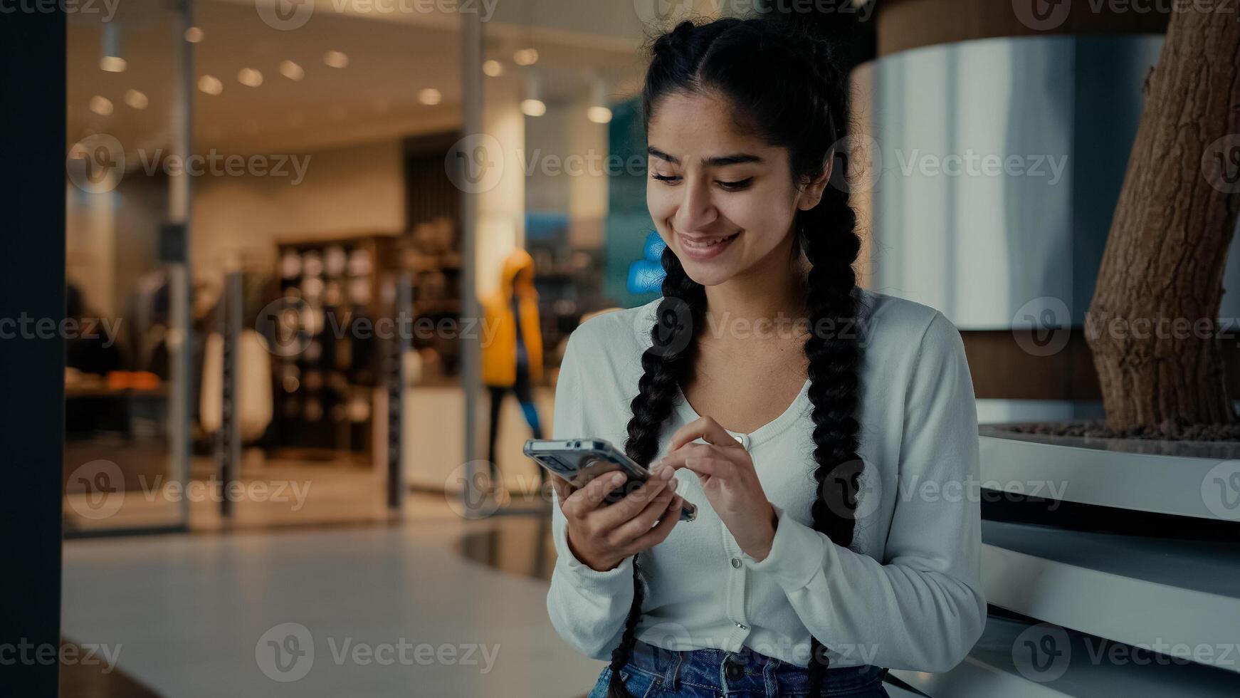 Attractive arabian young woman student middle-eastern girl sit at shopping mall look at screen texting message to business chat make order in internet store use mobile phone for distant communication photo