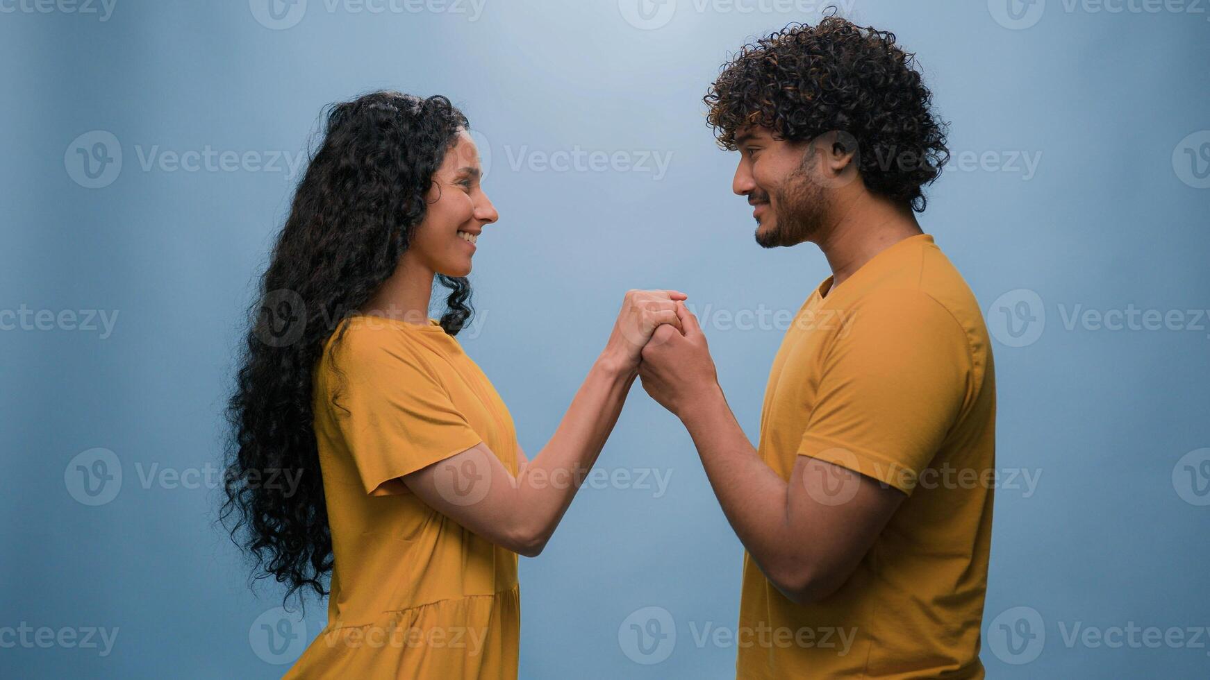 Happy couple love multiracial relationships affectionate date weeding married Latino woman Hispanic wife girlfriend holding hands with Indian man Arabian husband boyfriend at blue studio background photo