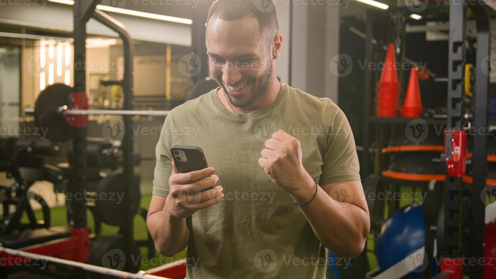 Excited happy African American trainer gym instructor guy sportsman male athlete bodybuilder man in sport club champion winner with mobile phone winning online prize achieve good news sports bet win photo