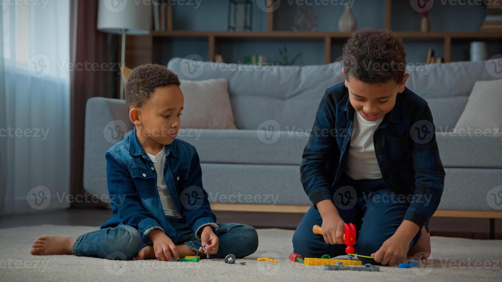 Two African American brothers little ethnic boys children siblings friends kids at home floor in living room playing with toy tools repairing building with hammer having fun busy play game with toys photo