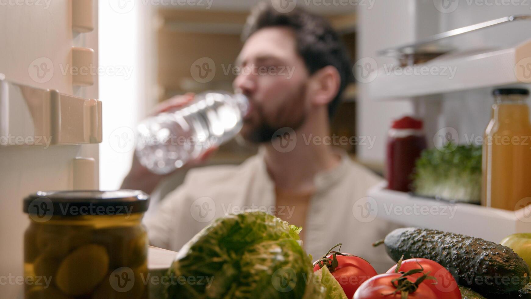 Point of view POV inside refrigerator Caucasian man male homeowner householder vegetarian guy open fridge with products vegetables at kitchen take out bottle with cold water drinking refreshment drink photo
