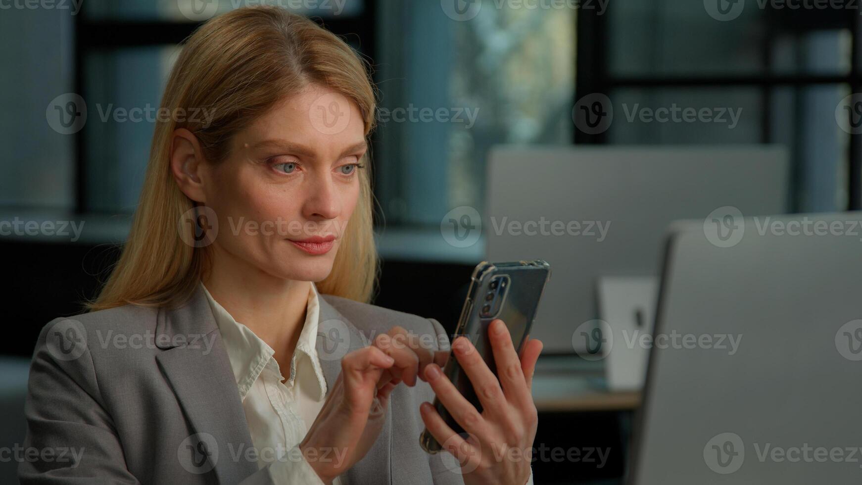 Caucasian middle-aged adult woman mature business female lady businesswoman entrepreneur scrolling browsing mobile phone win winning gesture celebrate achievement success online bet prize in office photo