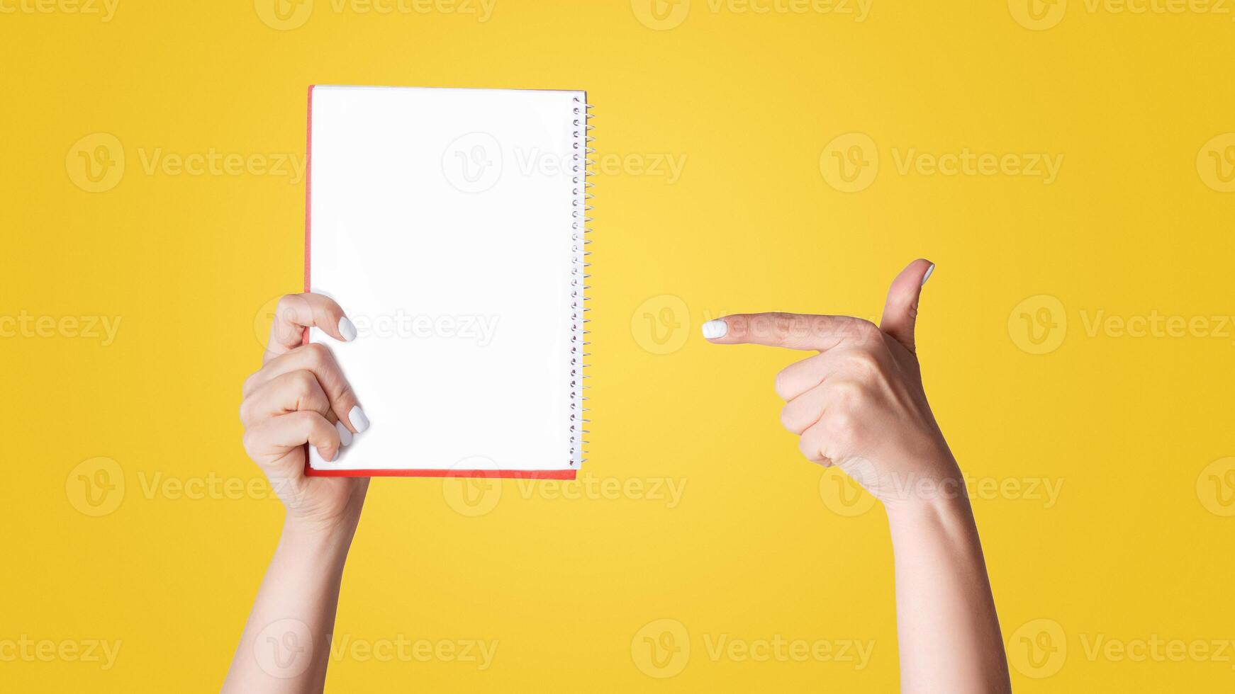 Woman pointing at empty notebook on light background, closeup. Mockup for design photo