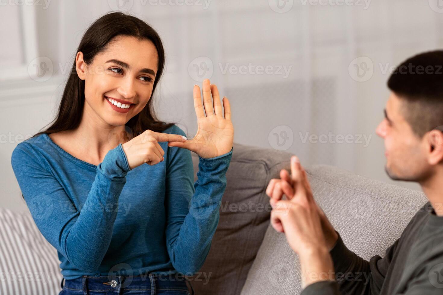 Smiling deaf and mute couple communicating at home using sign language, sitting on couch in living room photo